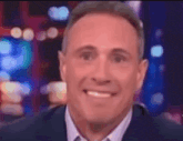 a man in a suit and tie is smiling and looking at the camera with a blurry background .