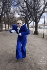 a man in a blue suit is dancing in a park with trees in the background