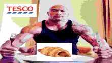 a muscular man is sitting at a table with a plate of food and a tesco logo behind him