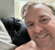 a man without a shirt is smiling with a black dog laying on his lap