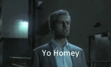 a man in a suit and white shirt is standing in a dark room with the words yo homey above him .