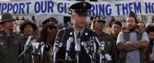 a man in a military uniform stands in front of microphones in front of a banner that says support our gis