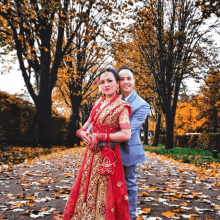 a bride and groom pose for a picture in front of trees with leaves on the ground