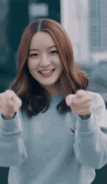 a woman in a blue sweater is smiling and pointing at the camera with her fist in the air .