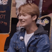 a young man in a denim jacket is smiling while sitting in front of a sign that says ice cream