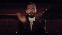 a man in a tuxedo and bow tie applauds in a theater
