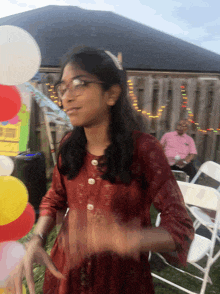 a girl wearing glasses is dancing in front of balloons and a sign that says ' a ' on it