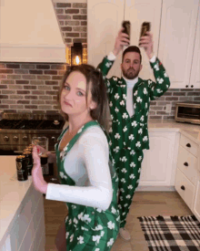 a man and a woman are dancing in a kitchen and the woman is wearing an apron with shamrocks on it