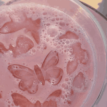 a close up of a pink drink with butterfly shaped ice cubes in it