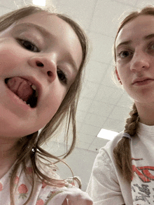 a little girl sticking her tongue out next to a girl wearing a white shirt