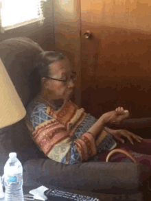 an elderly woman sits in a chair next to a lamp and a water bottle