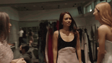 three women are standing in a room with clothes hanging on racks
