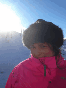 a woman wearing a pink jacket and a black hat stands in the snow