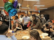 a group of people are eating pizza and balloons are hanging from the ceiling