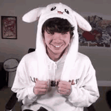 a young man wearing a white bunny hat and a white hoodie is smiling .