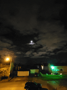 a car is parked in a driveway at night with a full moon in the sky