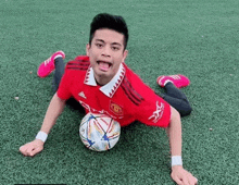 a man in a red adidas shirt is laying on the grass with a soccer ball in his lap