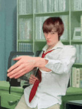 a young man in a white shirt and red tie is dancing in front of a bookshelf