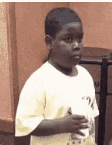 a young boy in a white shirt is standing in front of a trash can and holding a cup .