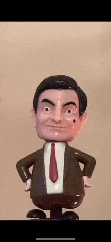 a bobble head of mr bean in a suit and tie is standing on a chair .