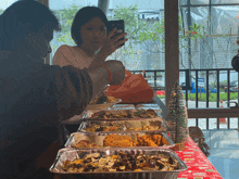 a woman taking a picture of a tray of food with her cell phone