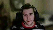a man wearing headphones and a red sweater is sitting in front of a computer .