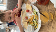 a young boy is eating a plate of food with a glass of orange juice