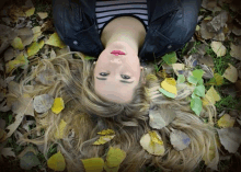 a woman laying in a pile of leaves with her eyes closed