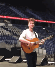 a man playing a guitar in front of an empty stadium with a banner that says la energia de las personas