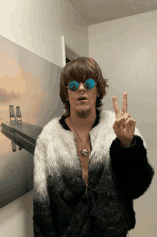 a man wearing sunglasses and a fur coat giving the peace sign