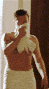 a shirtless man in a white towel wipes his face