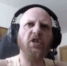 a bald man with a beard is wearing headphones and looking at the camera .