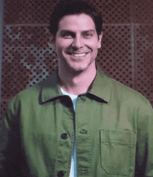 a man wearing a green jacket is smiling and looking at the camera .