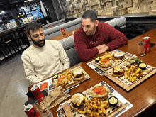 two men sitting at a table with plates of food and a can of coca cola