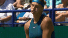 a woman in a blue nike tank top is sitting on a tennis court in front of a crowd .