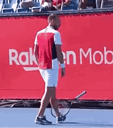 a man is holding a tennis racquet on a tennis court in front of a red banner that says rakuten mob .