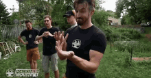 a group of men are standing in a backyard . one of the men is wearing a black shirt with an anvil on it .