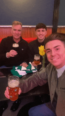 three men are sitting at a table holding up glasses of beer