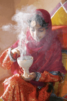 a woman in a red and gold dress is holding a bowl of smoke