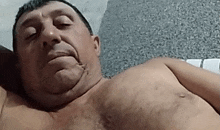 a shirtless man is laying on a bed with his eyes closed and his mouth open .