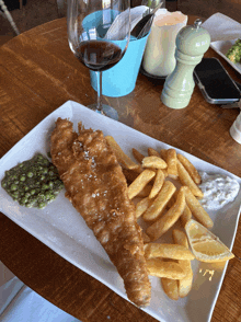 a plate of fish and chips on a table with a glass of wine in the background