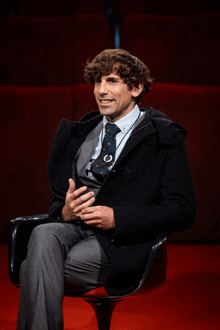 a man in a suit and tie is sitting in a chair and smiling