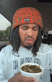 a man with dreadlocks wearing a t8a shirt is eating a bowl of food