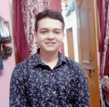 a young man in a blue shirt is standing in front of a door and smiling at the camera .