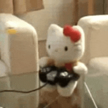 a stuffed hello kitty is sitting on a glass table holding a game controller .