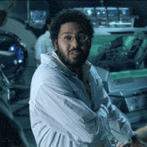 a man wearing glasses and a lab coat stands with his arms crossed in a dark room