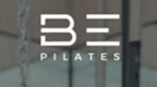 a logo for be pilates with a blurred image of a gym in the background .