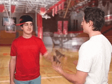 two young men are standing on a basketball court talking to each other