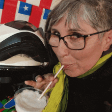 a woman wearing glasses and a yellow scarf drinks from a cup with a straw