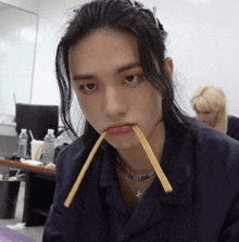 a young man with long hair is eating french fries with a toothpick in his mouth .